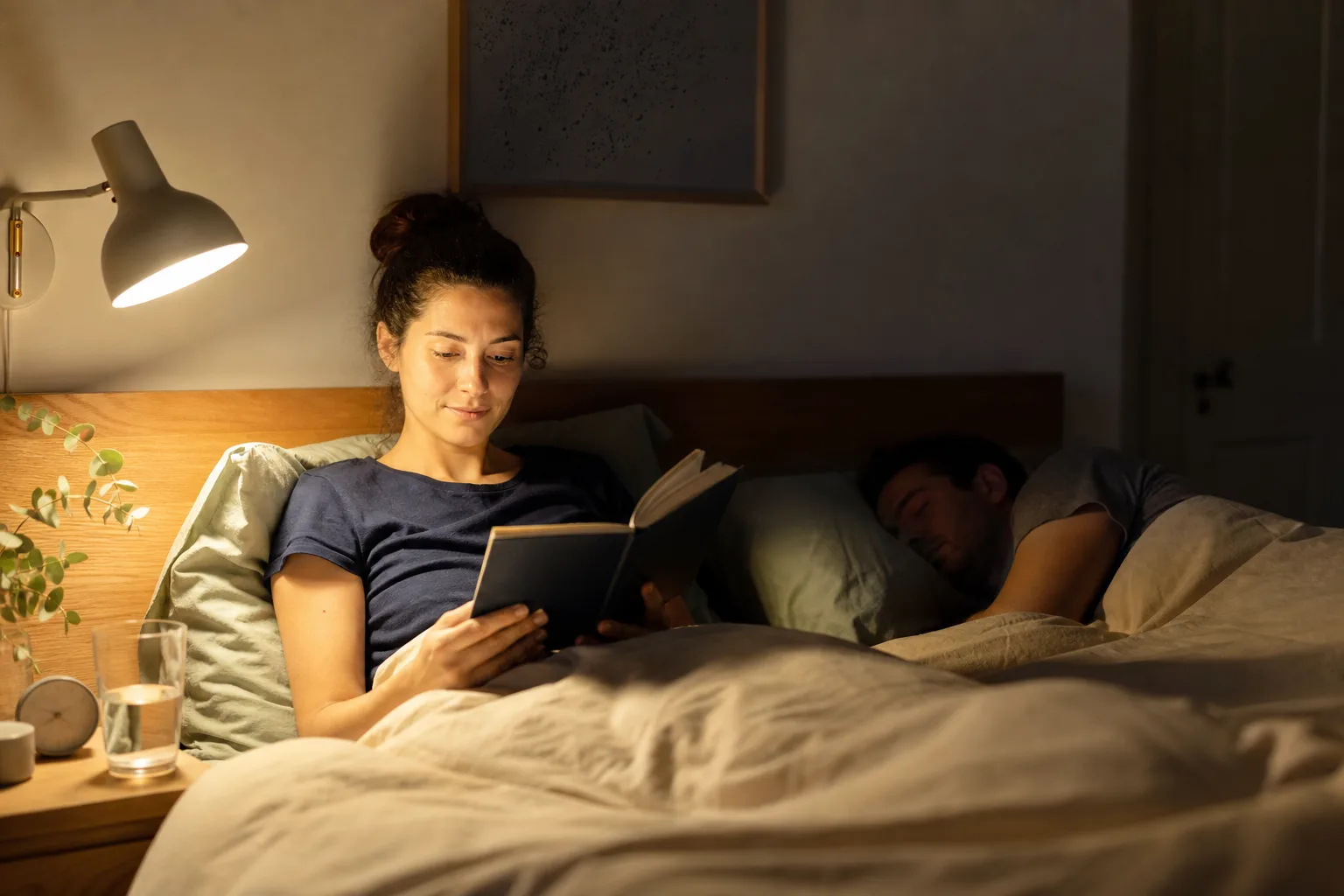 Focused bedside reading lamp lighting one side of a shared bed